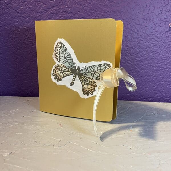 Gold booklet with butterfly illustration and ribbon.